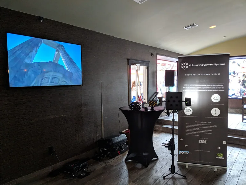 Wide view of VCS banner, compact camera and VR demo against a black wall.