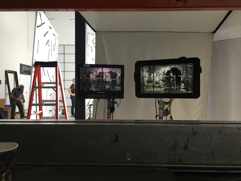 Two witness monitors seen across a workbench, with camera stage in background.