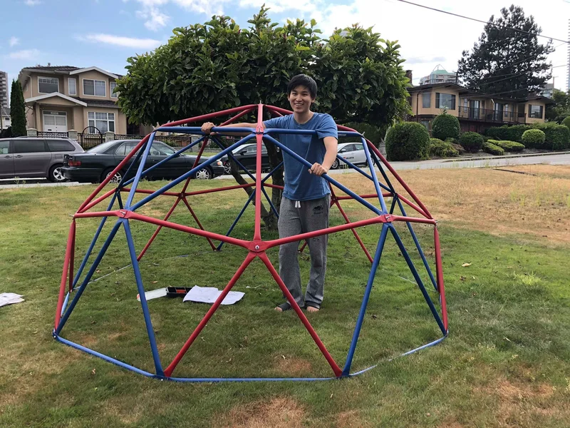 Person standing inside an early geodesic dome frame. The frame has not yet become a completed capture array.