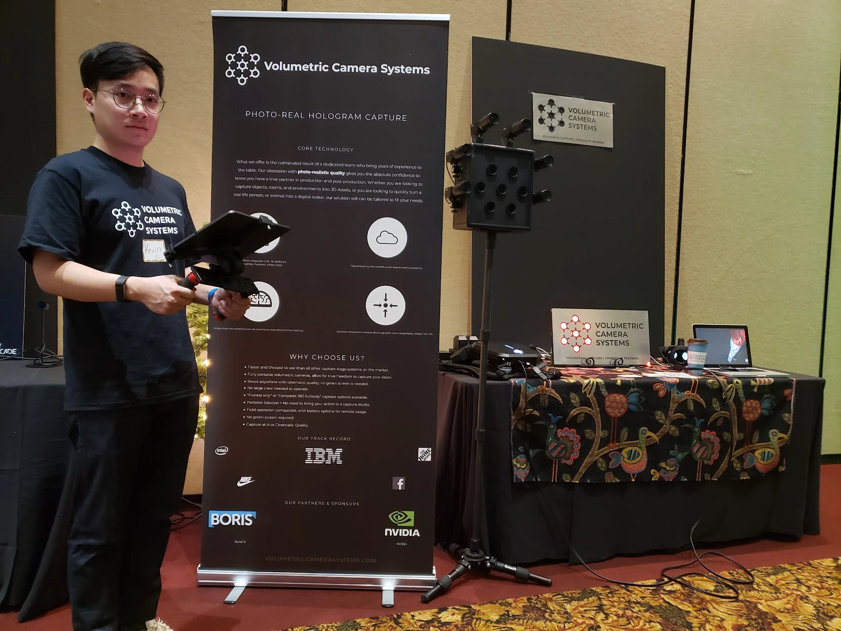 VCS operator holding a headset beside the compact camera, banner and monitor.