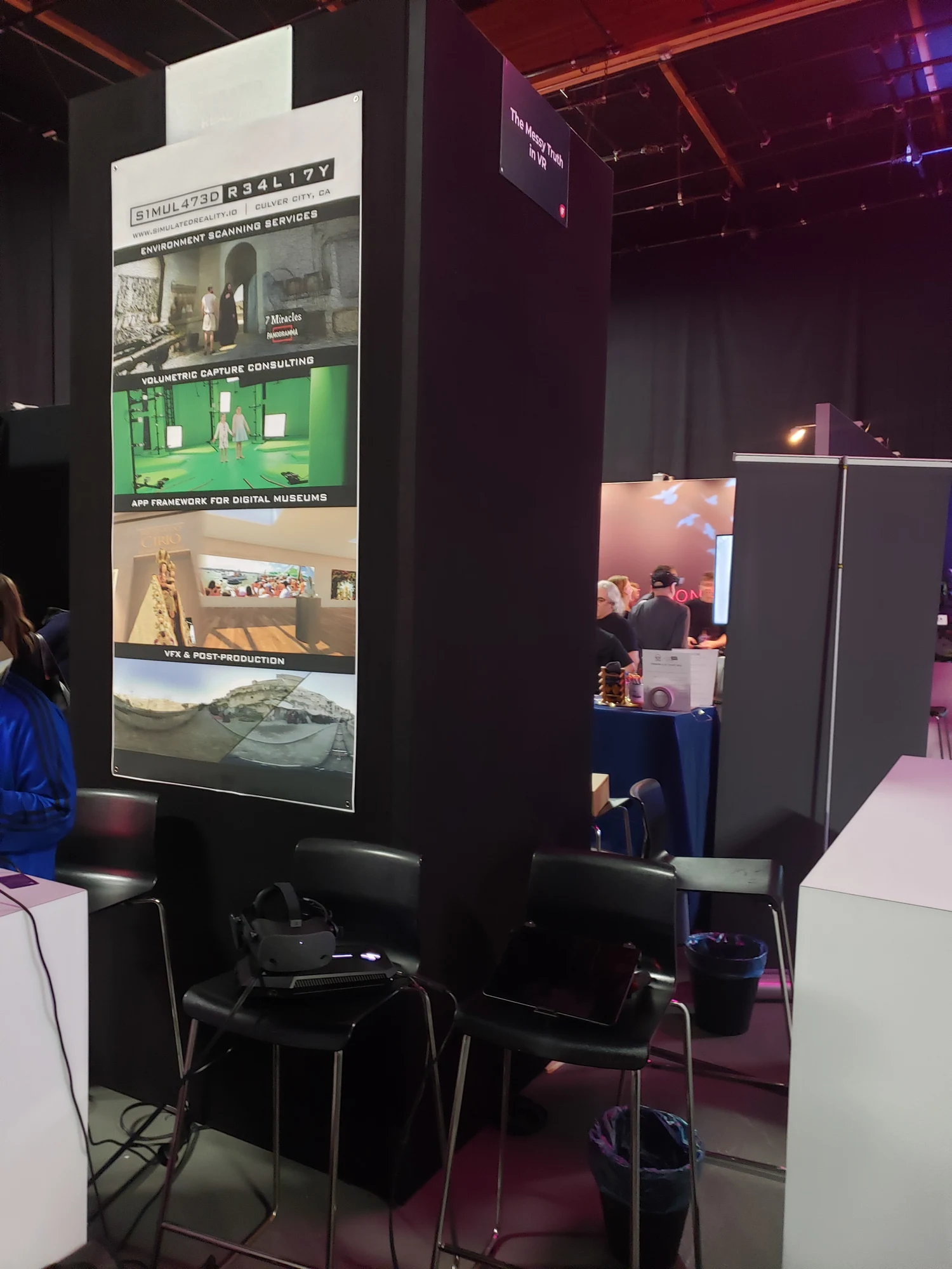 Portrait view of display screens, VR equipment and seating at the Simulated Reality partner booth.