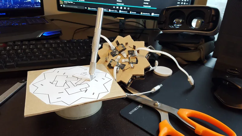 Early prototype assembly on desk: cardboard camera geometry, electronics, wiring and cutting pattern.