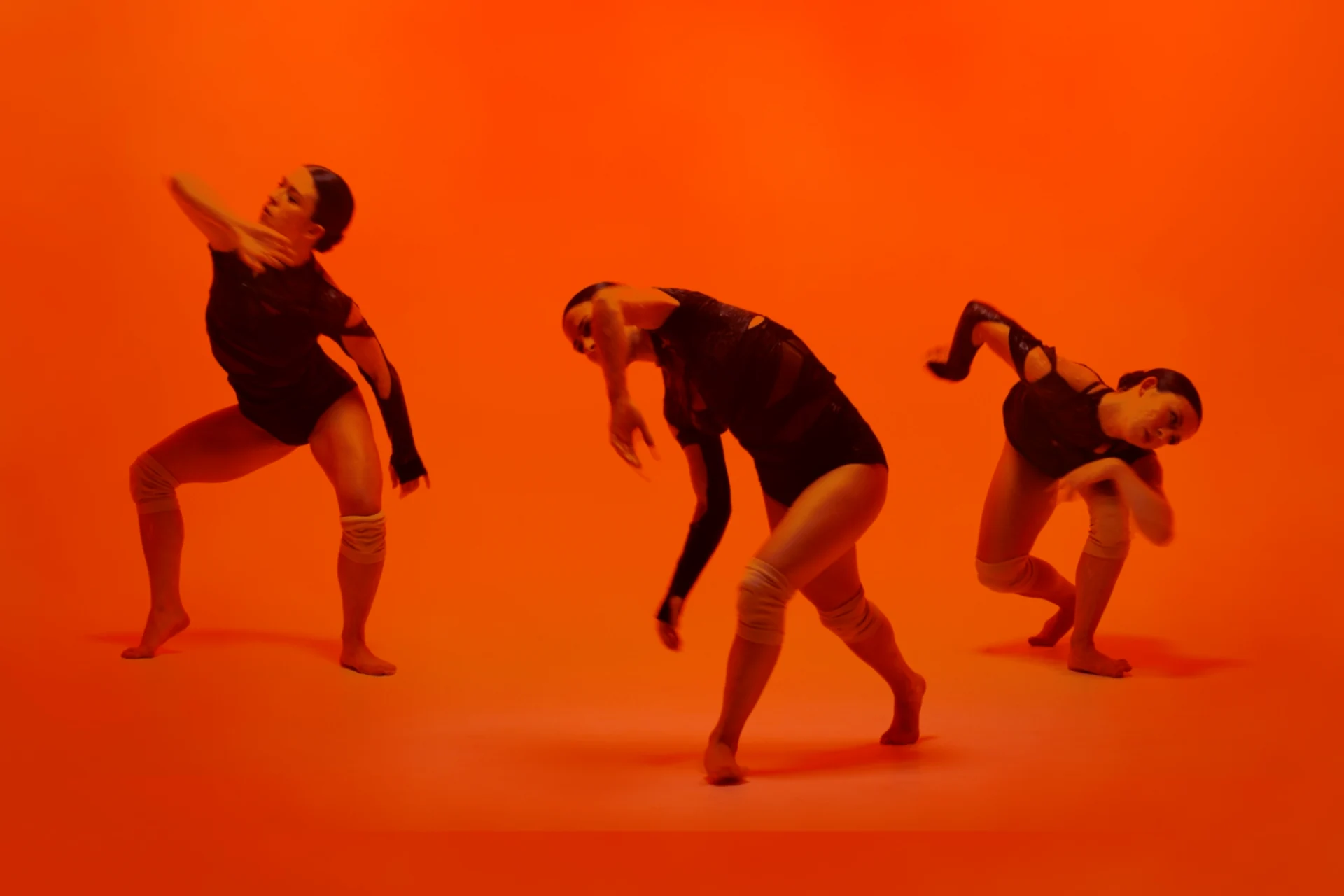 Metamorphosis film still: a dance composition against an orange field.